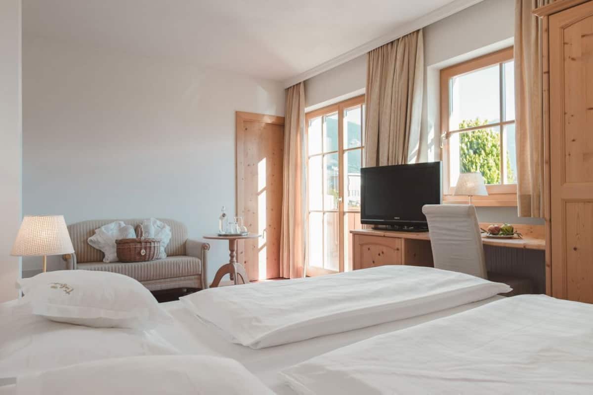 A hotel room with a bed, a desk with a TV, a chair, a lamp, and a window with curtains.