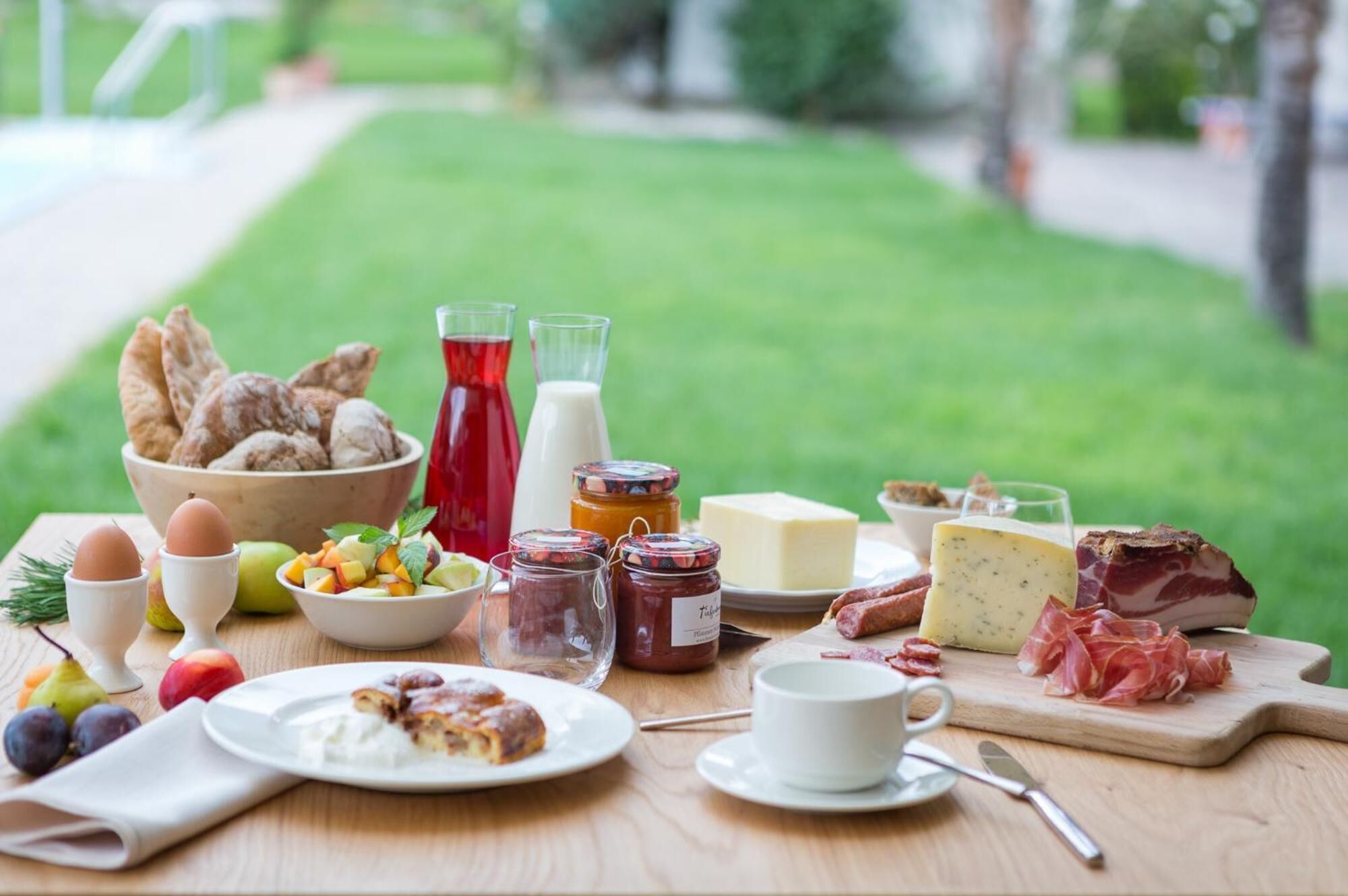 A breakfast table with bread, eggs, fruit, cheese, and meats.