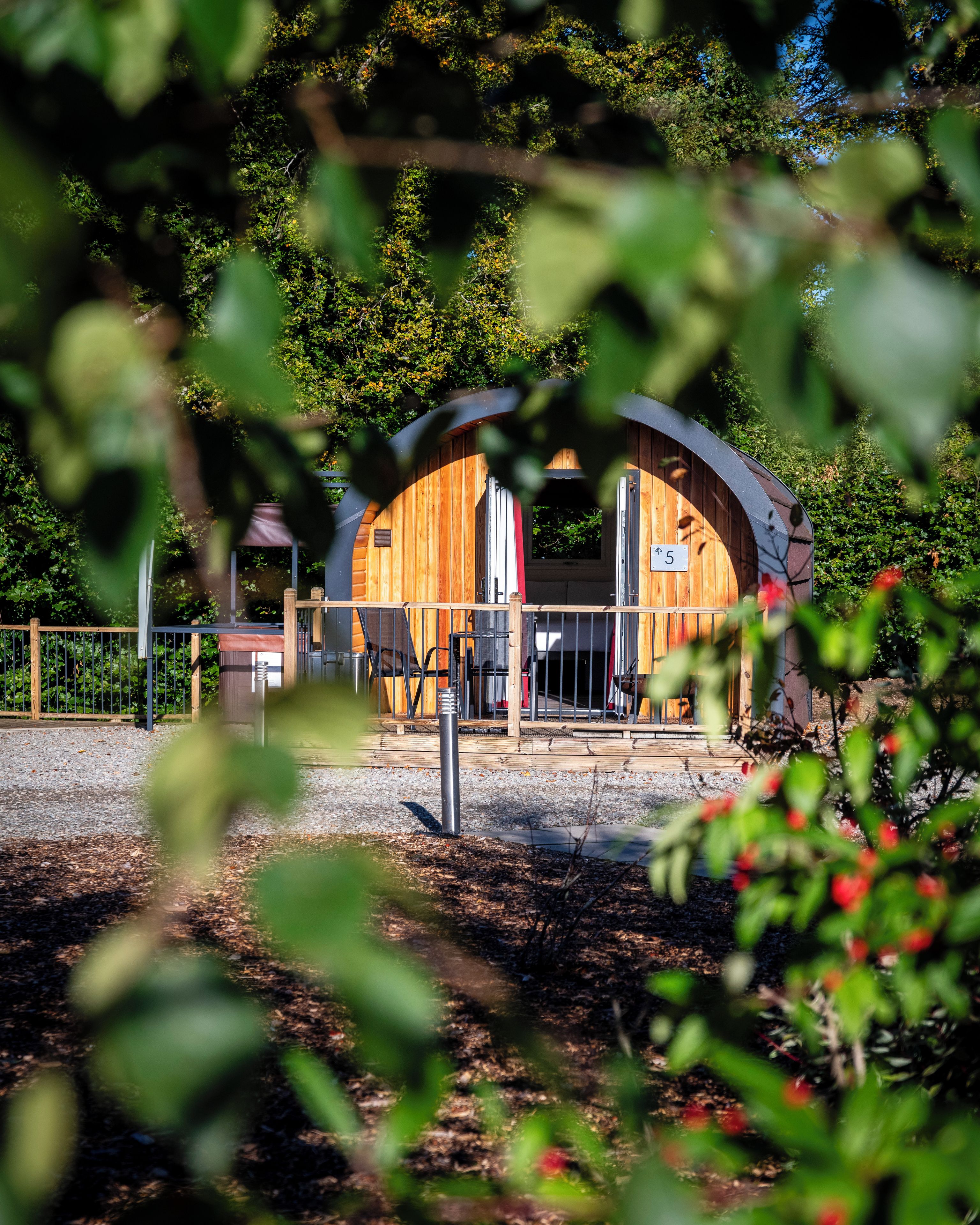 A wooden cabin with a curved roof, a fenced patio area, and a number sign indicating its location.