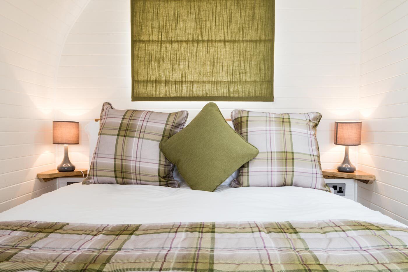A neatly made bed with plaid bedding, two bedside lamps, and a wall-mounted light fixture.