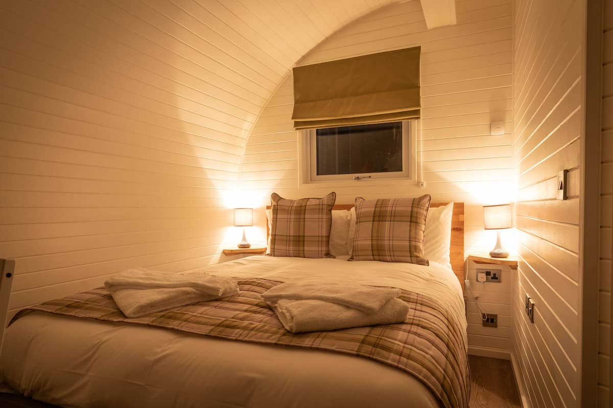 A cozy bedroom with a bed, two bedside lamps, a window with a blind, and a nightstand with a lamp.