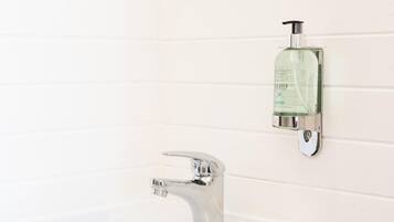 Un baño con pared de azulejos blancos, grifo cromado y dispensador de jabón montado en la pared.