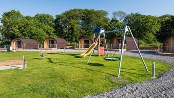 Un parque infantil con columpios y un tobogán, rodeado de estructuras de madera con ventanas.