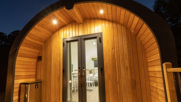 A wooden cabin with a glass door, a small outdoor seating area, and a wooden deck. - Weedingshall Lodges (Falkirk)