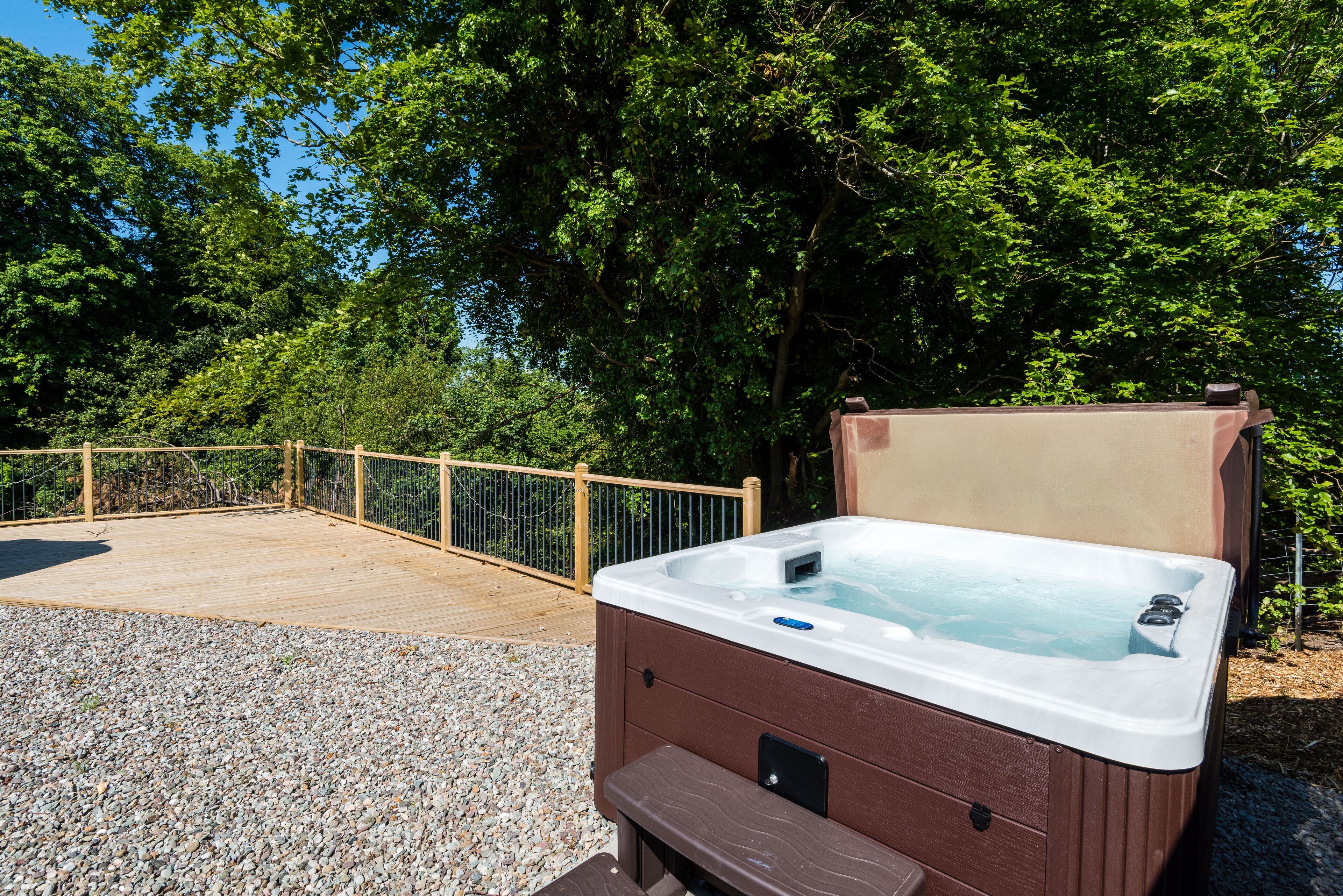 Un jacuzzi en una terraza de madera, con una valla de madera y árboles al fondo.