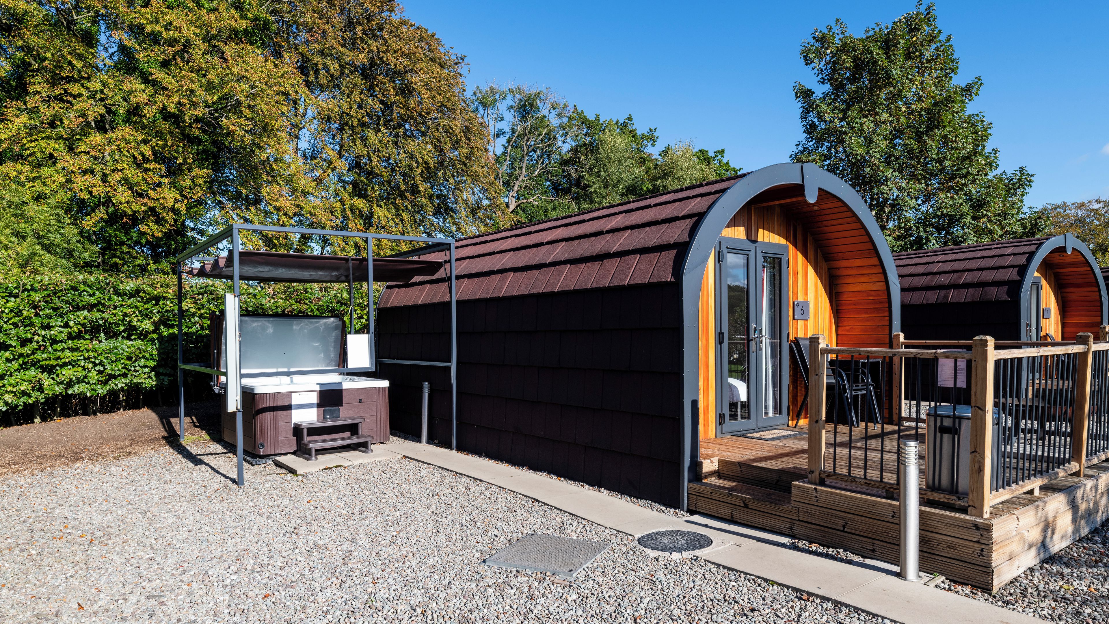 Ein kleines, eingeschossiges Gebäude mit überdachter Terrasse, Whirlpool und Holzterrasse.