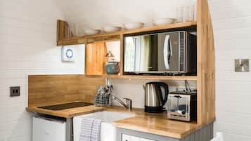 A compact kitchen with a wooden countertop, a sink, a kettle, a toaster, and a microwave.