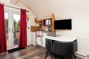 Une cuisine compacte avec un coin repas, un téléviseur fixé au-dessus du comptoir et un rideau rouge sur la porte.