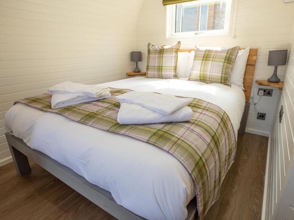A neatly made bed with a plaid bedspread and pillows, a bedside table with a lamp, and a window above the bed.