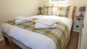 A neatly made bed with a plaid bedspread and pillows, a bedside table with a lamp, and a window above the bed.