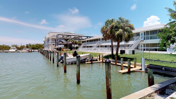 Una propiedad frente al agua con muelle, un bote y un edificio con balcón con vista al agua.