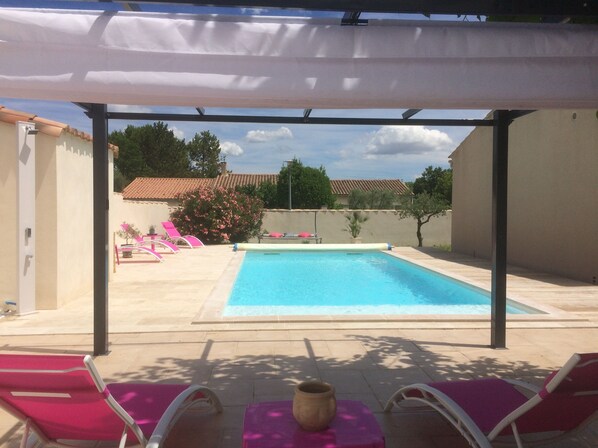 A covered outdoor swimming pool with lounge chairs and a potted plant.