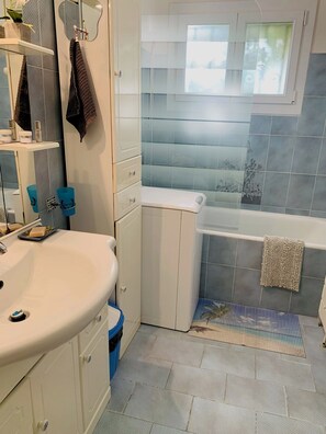 A bathroom with a white sink, a bathtub, and a window.