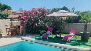 Een zwembad met twee roze ligstoelen en een tafel onder een grote parasol.