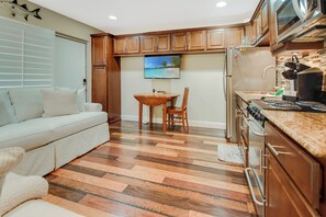A compact kitchen with wooden cabinets, a dining area, and a living space with a sofa.