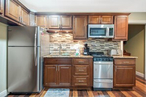 A kitchen with wooden cabinets, a stainless steel refrigerator, a microwave, a stove, and a sink.