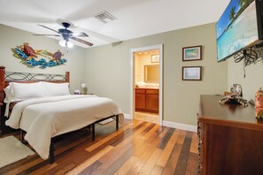 A bedroom with a bed, wooden flooring, a ceiling fan, a wall-mounted turtle decoration, and a door leading to a bathroom. - Driftwood Landing 13- Isles of Capri Vacation Resort. (Naples)
