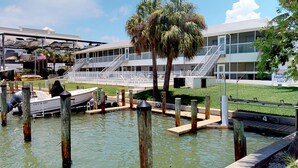 Un port de plaisance avec des bateaux amarrés, un bâtiment doté d’un balcon et une zone herbeuse avec des escaliers menant au bâtiment.