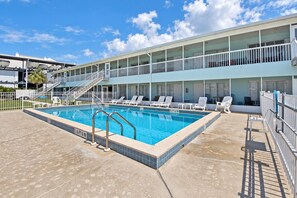 A hotel with a swimming pool, outdoor seating, and a covered area with stairs leading to the upper floors.