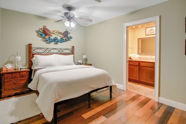 Un dormitorio con cama de madera, mesita de noche, un adorno en la pared y ventilador de techo.