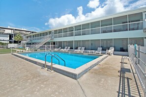 Una piscina con tumbonas y un edificio de varios pisos con balcones.