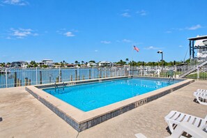 A rectangular swimming pool with a tiled edge, a flagpole with an American flag, and a white fence surrounding the pool.