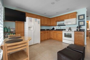 A kitchen with wooden cabinets, a refrigerator, a microwave, a stove, and a dining area with chairs and a table.