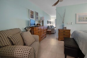 A well-lit, spacious room with a bed, a sofa, a desk with a computer, and a dresser.