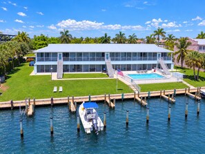 A modern two-story building with a swimming pool, docked boat, and a well-maintained lawn.