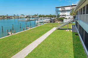 Un puerto deportivo con barcos amarrados, un área con césped y un edificio con balcón con vistas al agua.