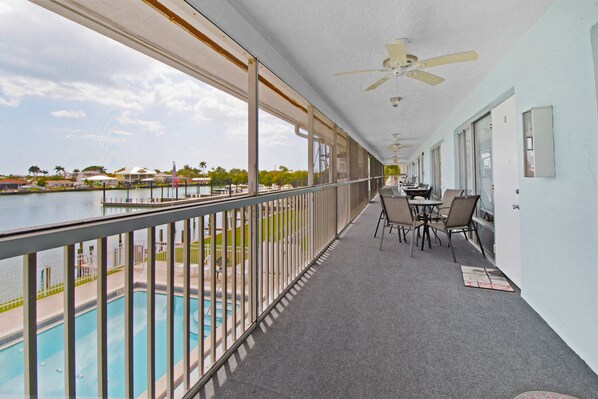 A balcony with a pool view, a ceiling fan, and a table with chairs.