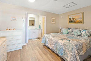 Un dormitorio con cama, cómoda y baño con lavamanos y espejo.