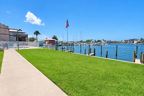 A marina with boats docked, a grassy area, a pathway, and a building with a flag.