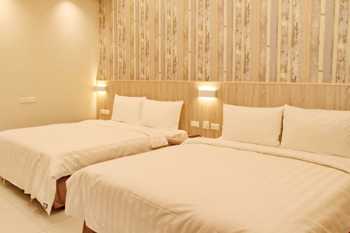 A hotel room with two beds, wooden headboard, and wall-mounted lights.