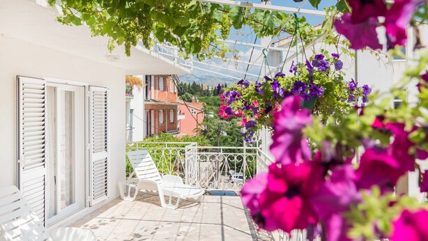 Un balcon avec des chaises blanches, une balustrade blanche et des fleurs violettes en suspension.
