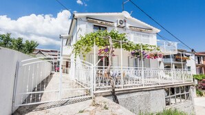 Un bâtiment blanc à deux étages, doté d’un balcon, d’un escalier et d’une porte blanche.