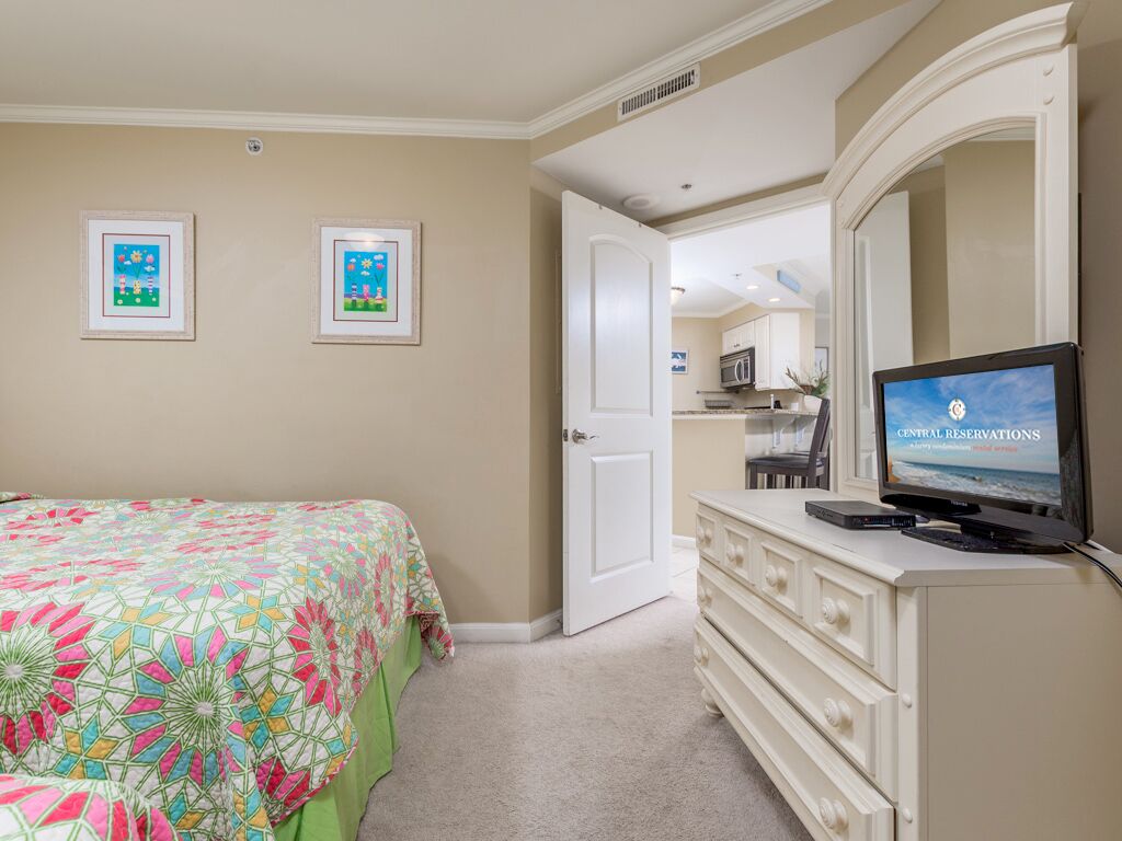 A bedroom with a bed, a dresser, a television displaying 'Central Reservations', and a door leading to a bathroom.