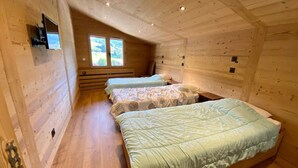 Een blokhut met drie bedden op rij, houten wanden en een raam dat voor natuurlijk licht zorgt.