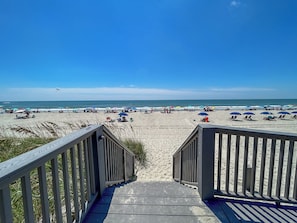 Eine Holztreppe führt zu einem Strand mit Sonnenschirmen und Liegestühlen.