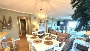 A dining area with a round table, white chairs, and a chandelier. - Tidemaster. 3 bedroom oceanfront condo 1st floor with elevator. Pool. (North Myrtle Beach)