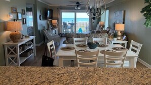 A dining area with a table set for four, a chandelier, and a view of the outdoors. - Tidemaster. 3 bedroom oceanfront condo 1st floor with elevator. Pool. (North Myrtle Beach)