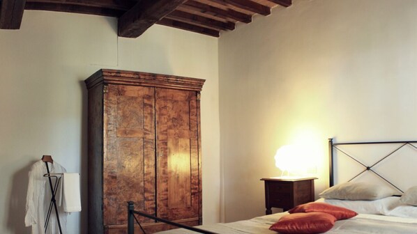 Een slaapkamer met een houten kledingkast, een nachtkastje met een lamp en een bed met kussens.