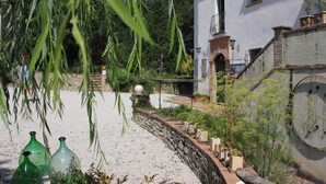 En have med en stenvæg, en hvid bygning med balkon, og grønne slyngplanter, der hænger ned.