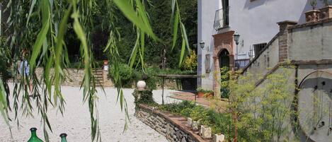 Un jardín con un muro de piedra, un edificio blanco con balcón y enredaderas verdes colgantes.