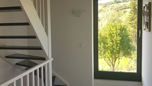 Eine Treppe mit weißen Geländern führt zu einer Zwischenebene, eine Tür mit grünem Rahmen und Blick auf eine von Bäumen gesäumte Landschaft.