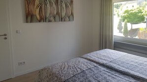 Ein Schlafzimmer mit einem Bett, einem Wandbild, einem Fenster mit Vorhängen und einer Tür mit Griff.