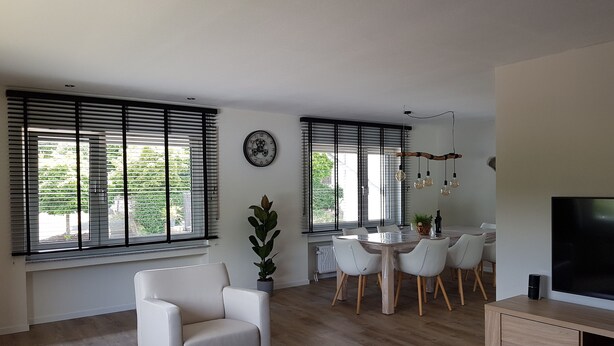 Ein modernes Wohnzimmer mit einem weißen Sofa, einem Essbereich mit einem Holztisch und Stühlen sowie einem Fernseher auf einer Holzkommode.