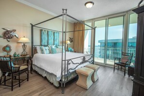 A four-poster bed with a balcony view, a wooden floor, and a seating area with chairs.
