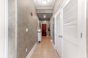 A hallway with a tiled floor, a white door with louvered panels, and a white console table with a decorative item.