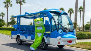 A mascot in a green frog costume standing next to a blue and white bus. - Peaceful Penthouse with Gulf Views! Complimentary Boat Slip! (Orange Beach)